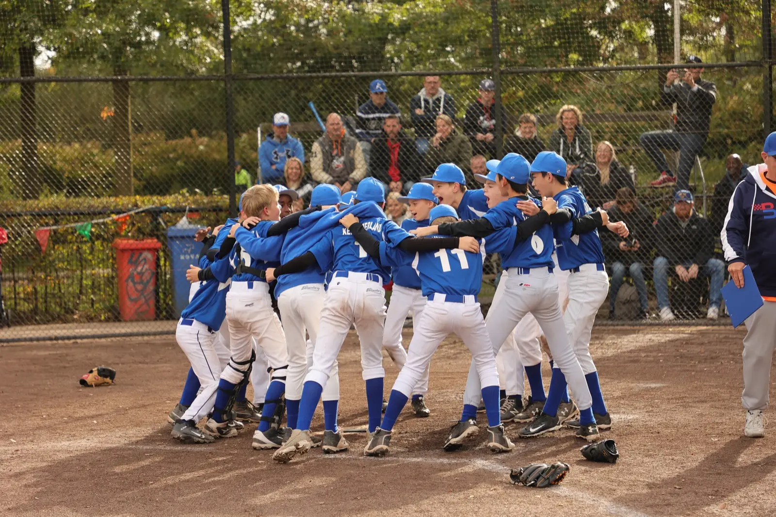 Een team staat in een kring met de armen om elkaar heen langs het hek.