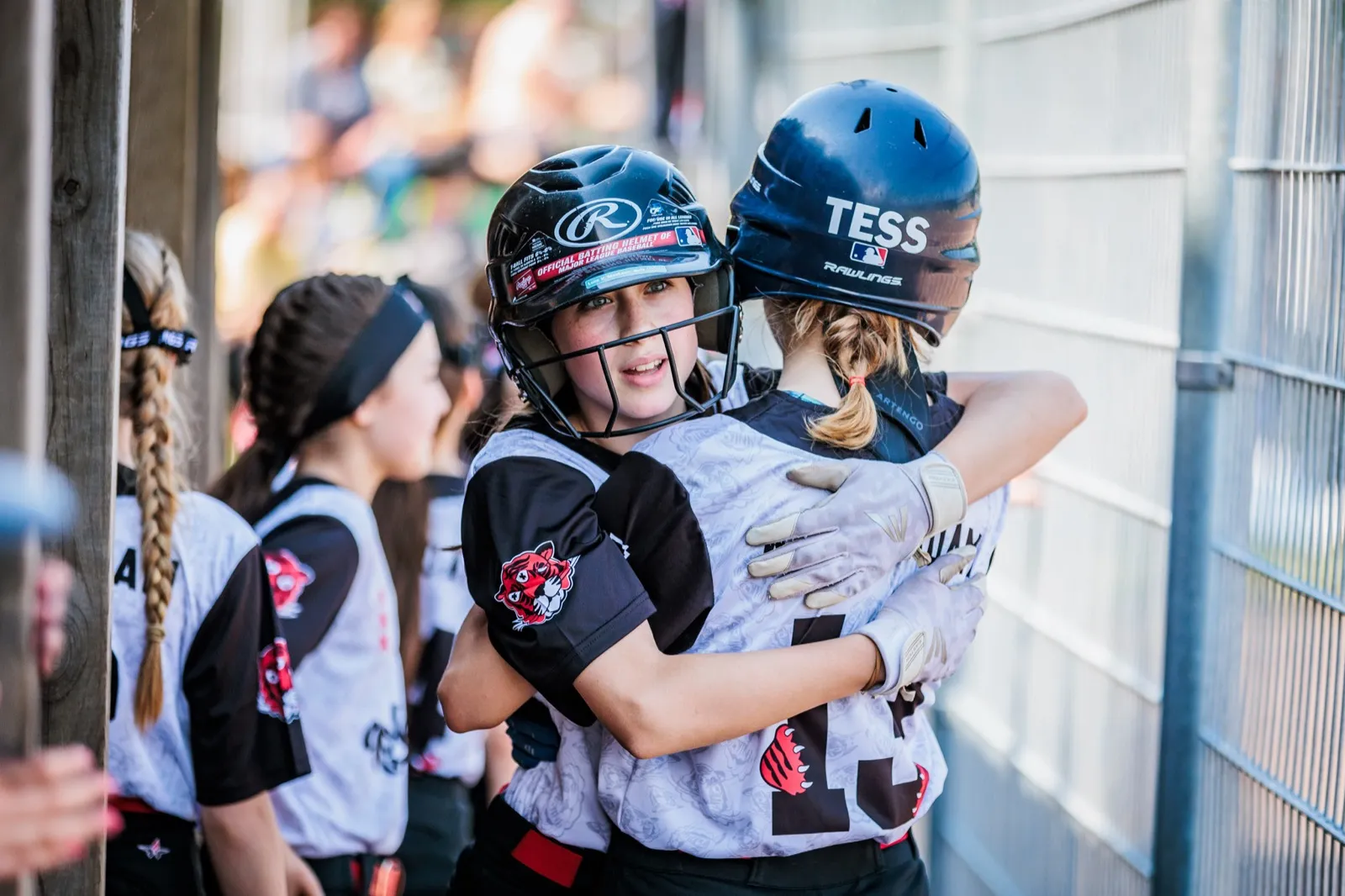 Twee softbalspeelsters omhelzen elkaar in de dug-out tijdens het NK Little League 2025.