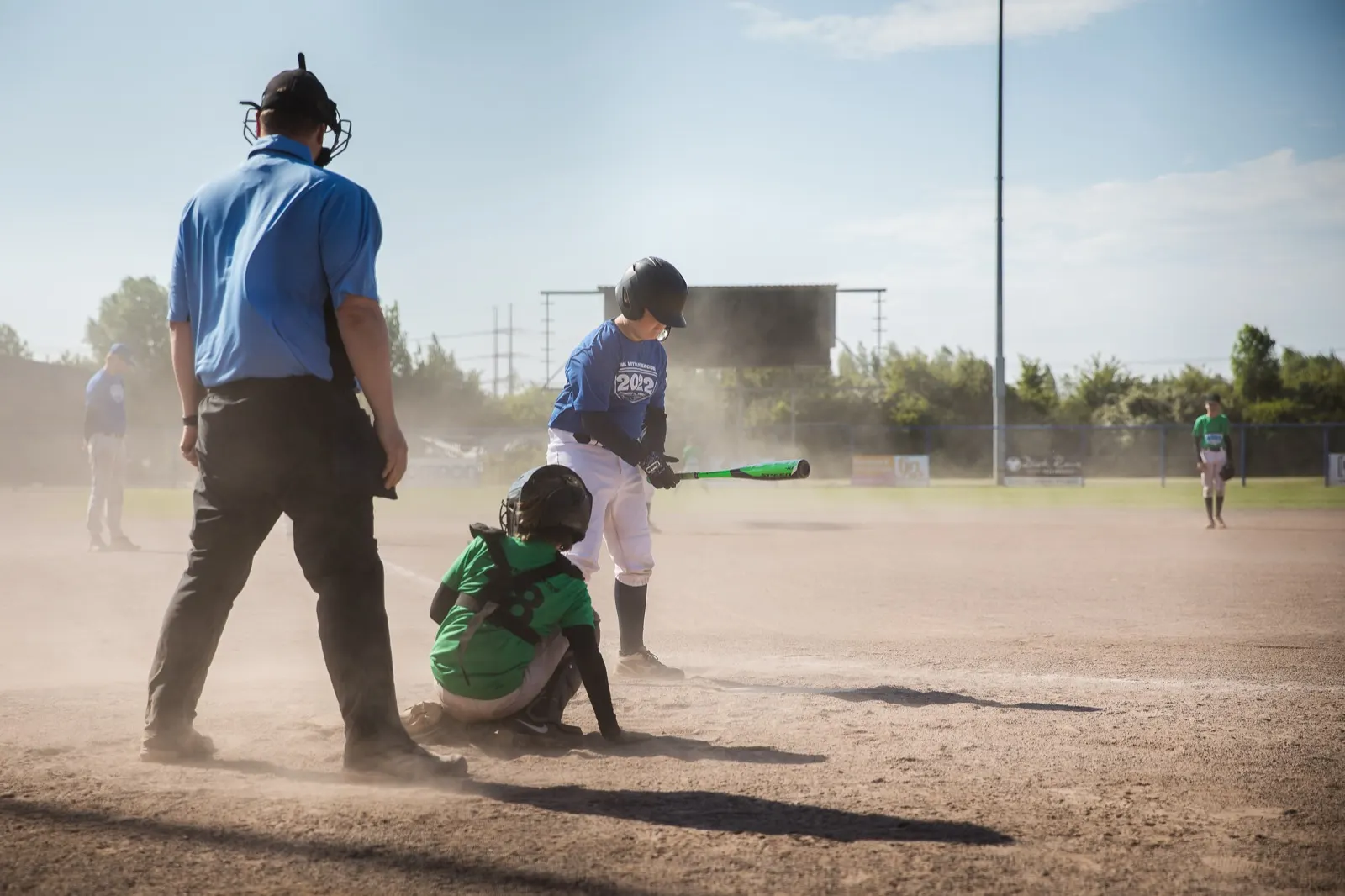 Een stofwolk rond de thuisplaat met umpire, slagman en catcher tijdens het NK Little League 2022.