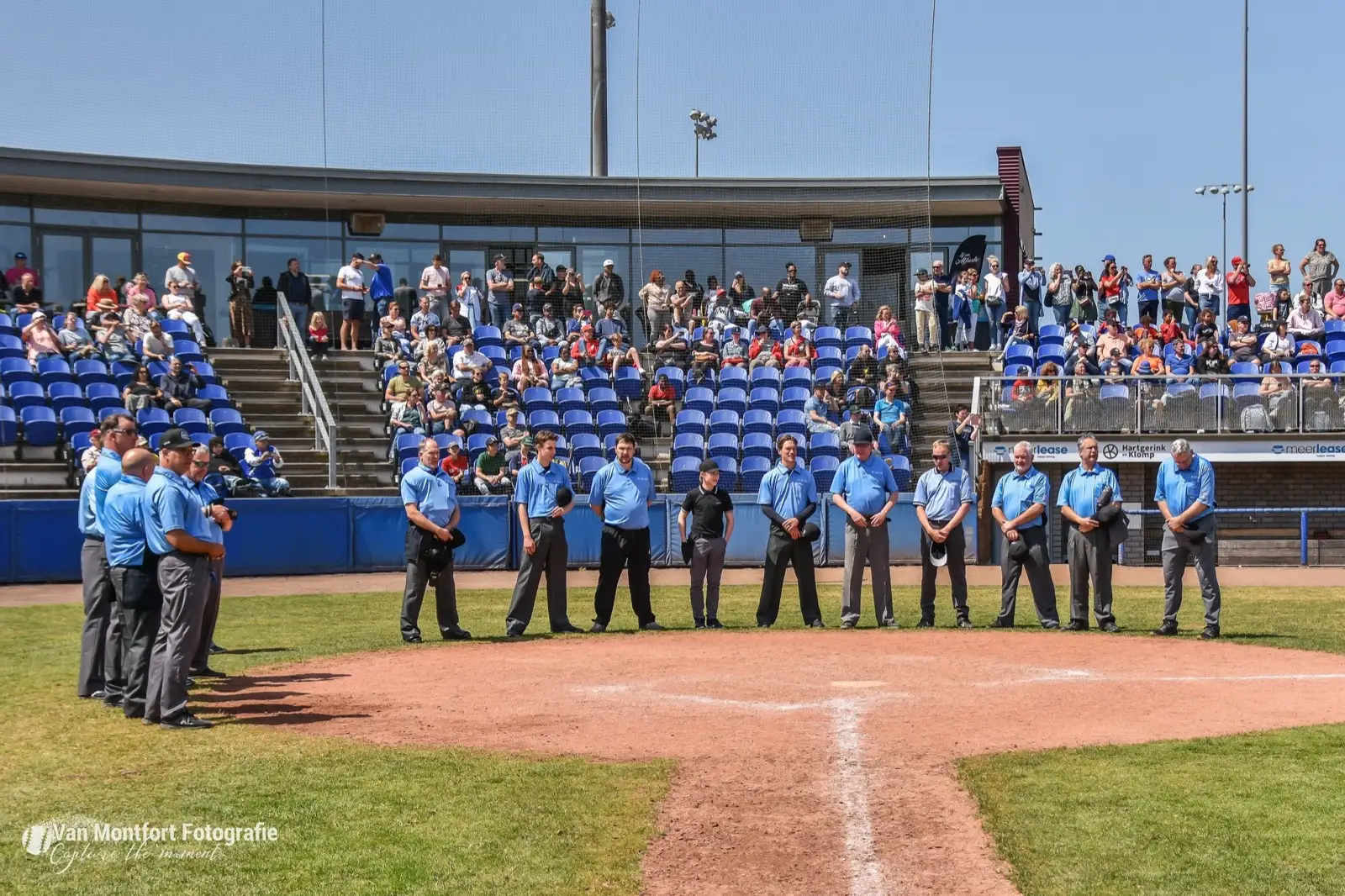 Umpires staan opgesteld rond de thuisplaat voor een volle tribune tijdens het NK Little League 2023.