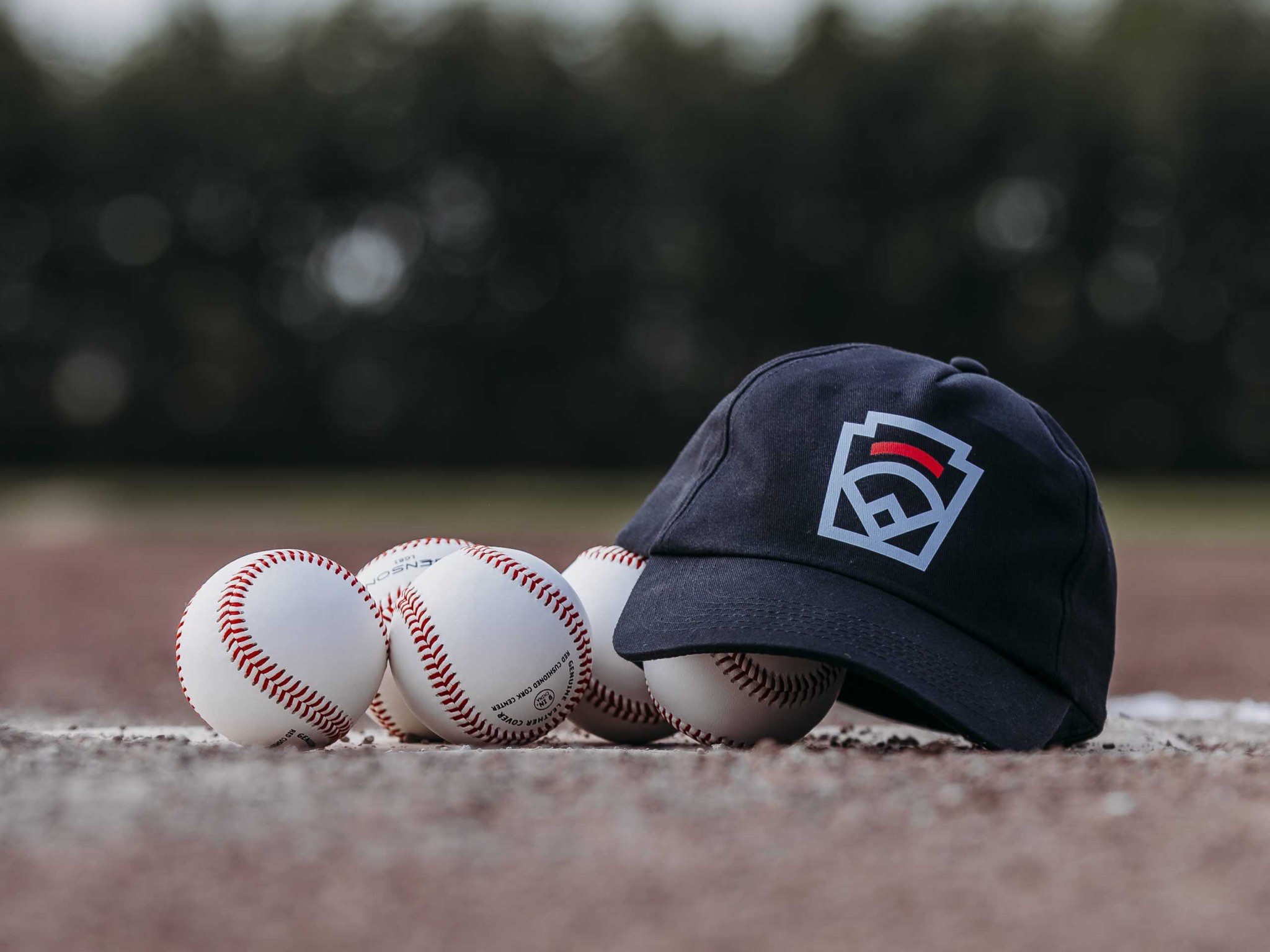 Vier honkballen naast een donkerblauwe Little League-pet op de rand van de thuisplaat.