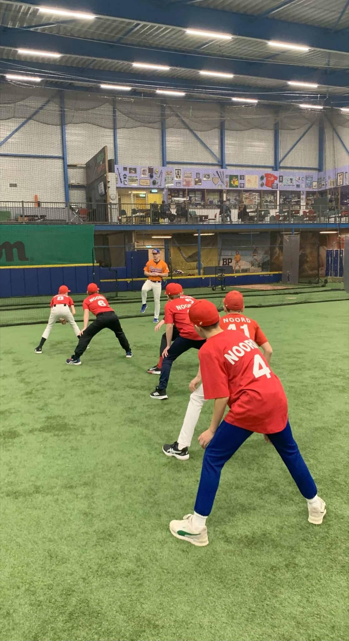 Jeugdspelers van Noord in rode shirts trainen op kunstgras in een indoorhal.