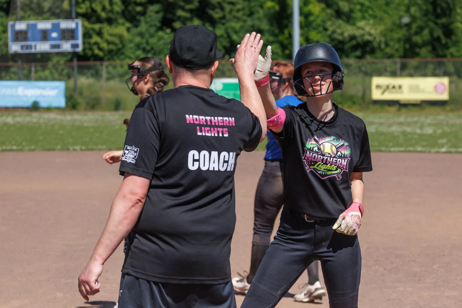 Een coach geeft een softbalspeelster met helm een high five op het veld.