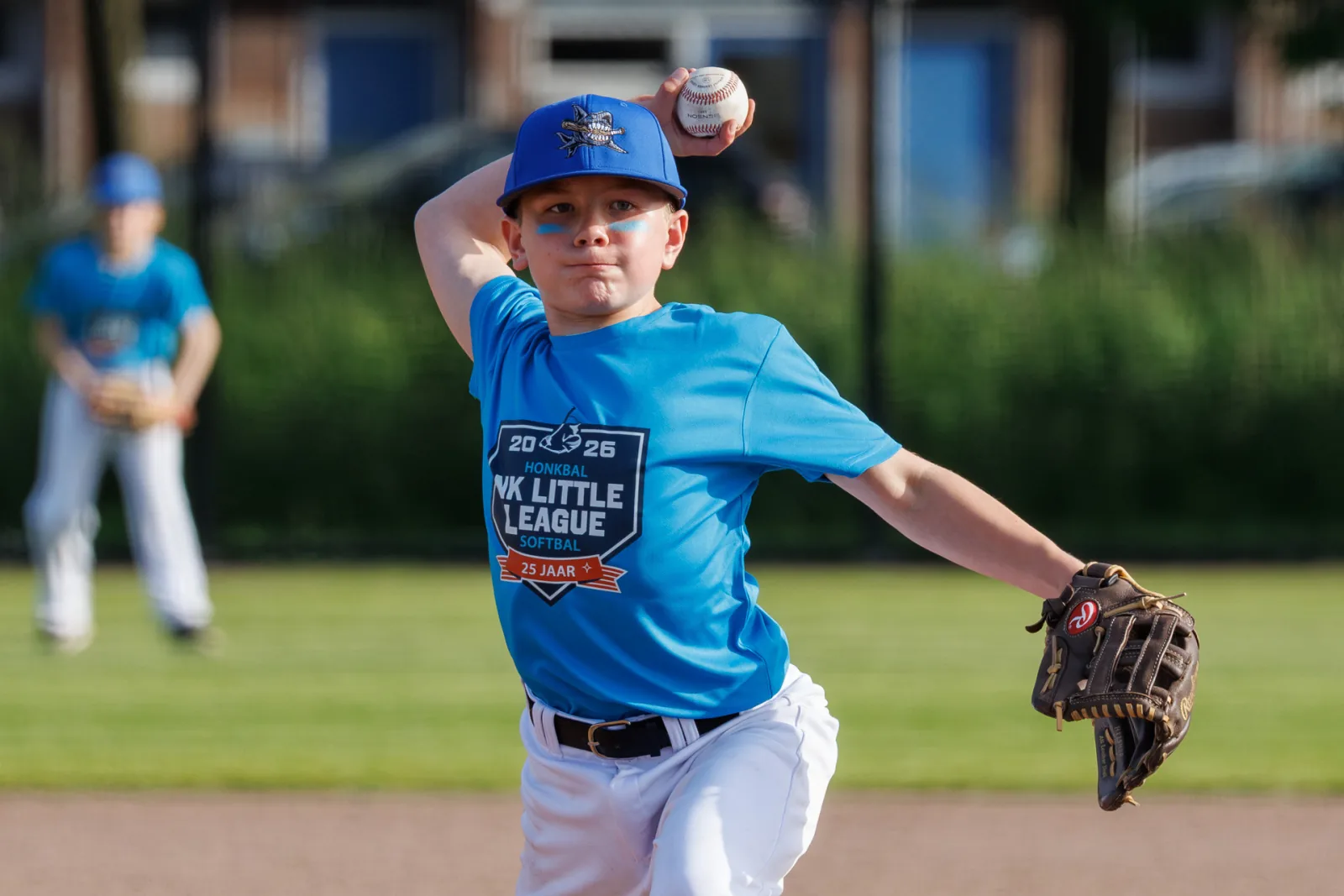 Jonge pitcher in het lichtblauwe NK-shirt haalt uit voor de worp.