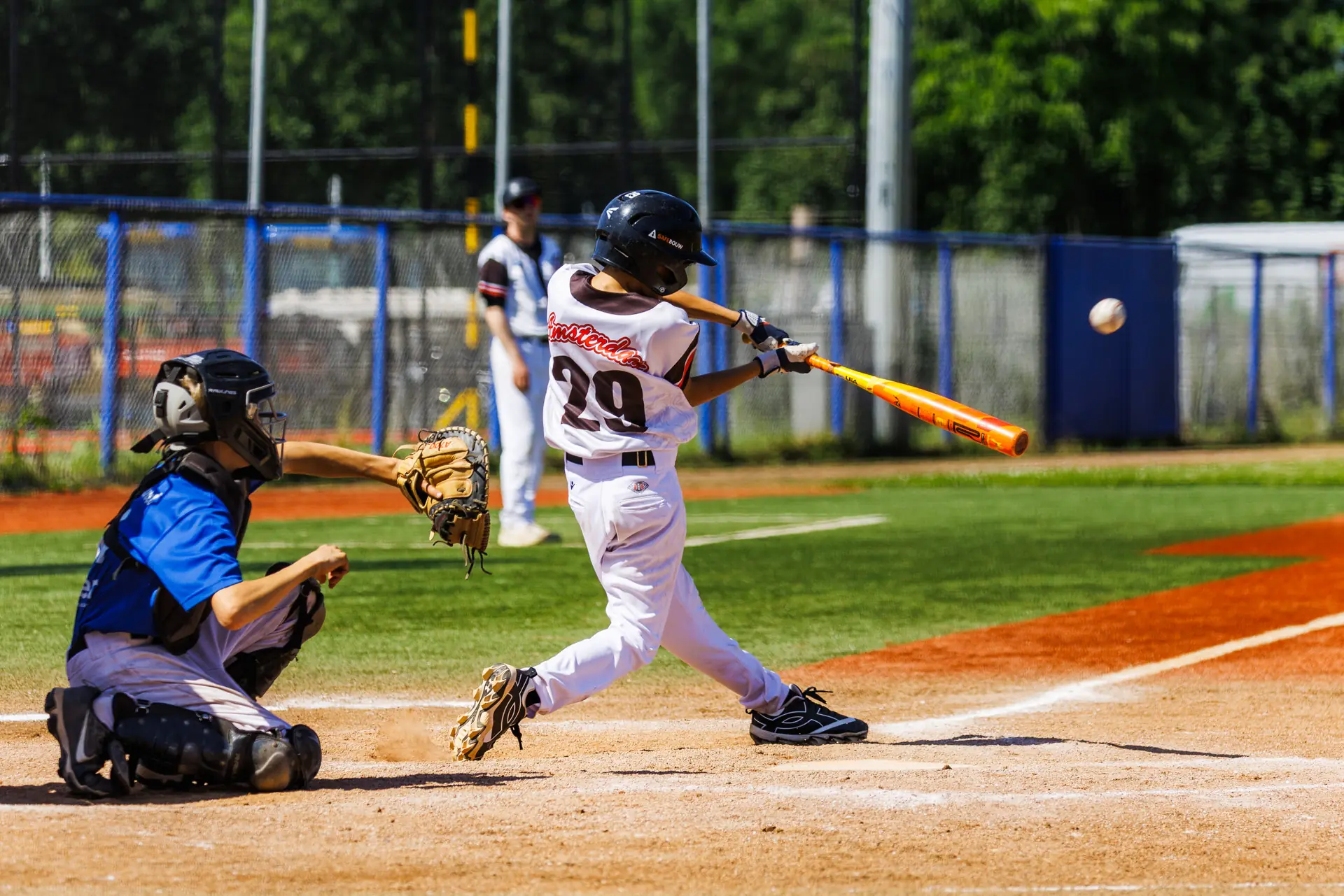 Honkballer raakt de bal, de catcher zit gehurkt achter de thuisplaat