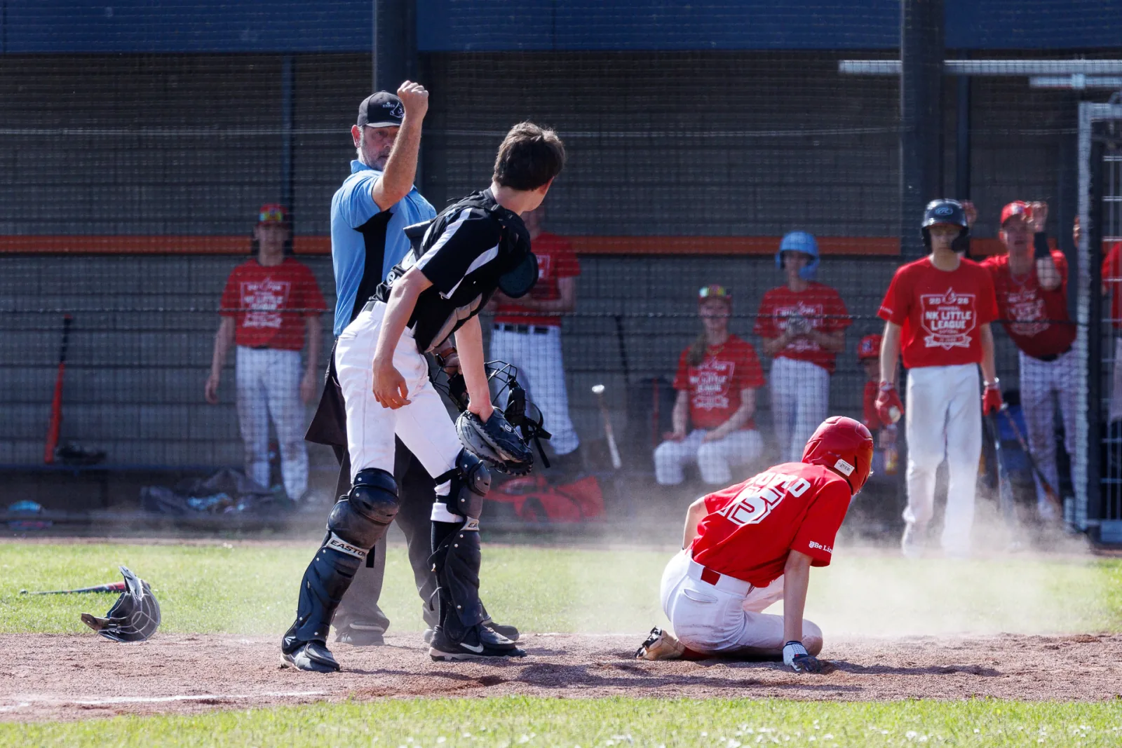Een honkballer glijdt door het stof naar de thuisplaat terwijl de catcher de bal opvangt.