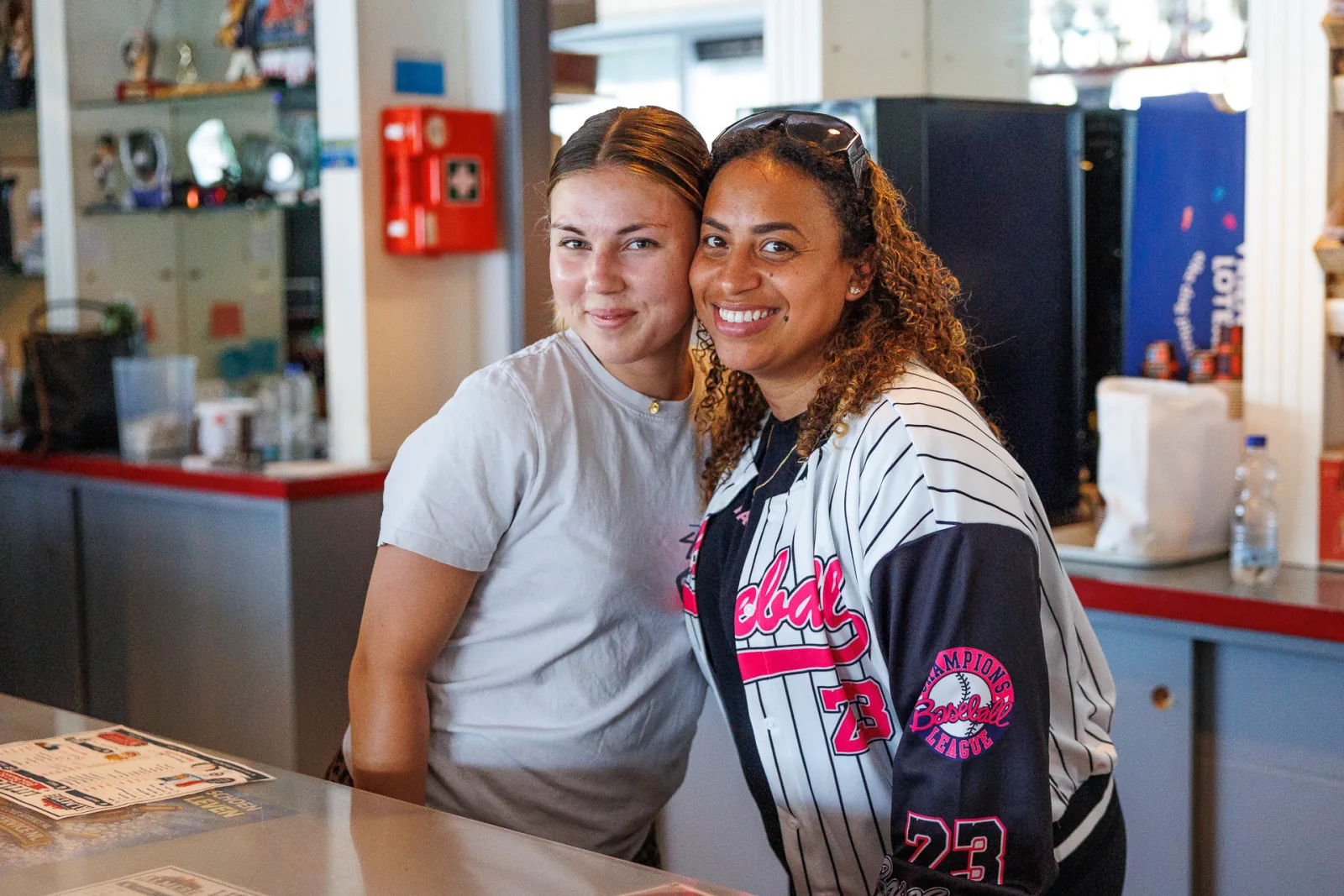 Twee vrijwilligers staan lachend naast elkaar in de kantine.