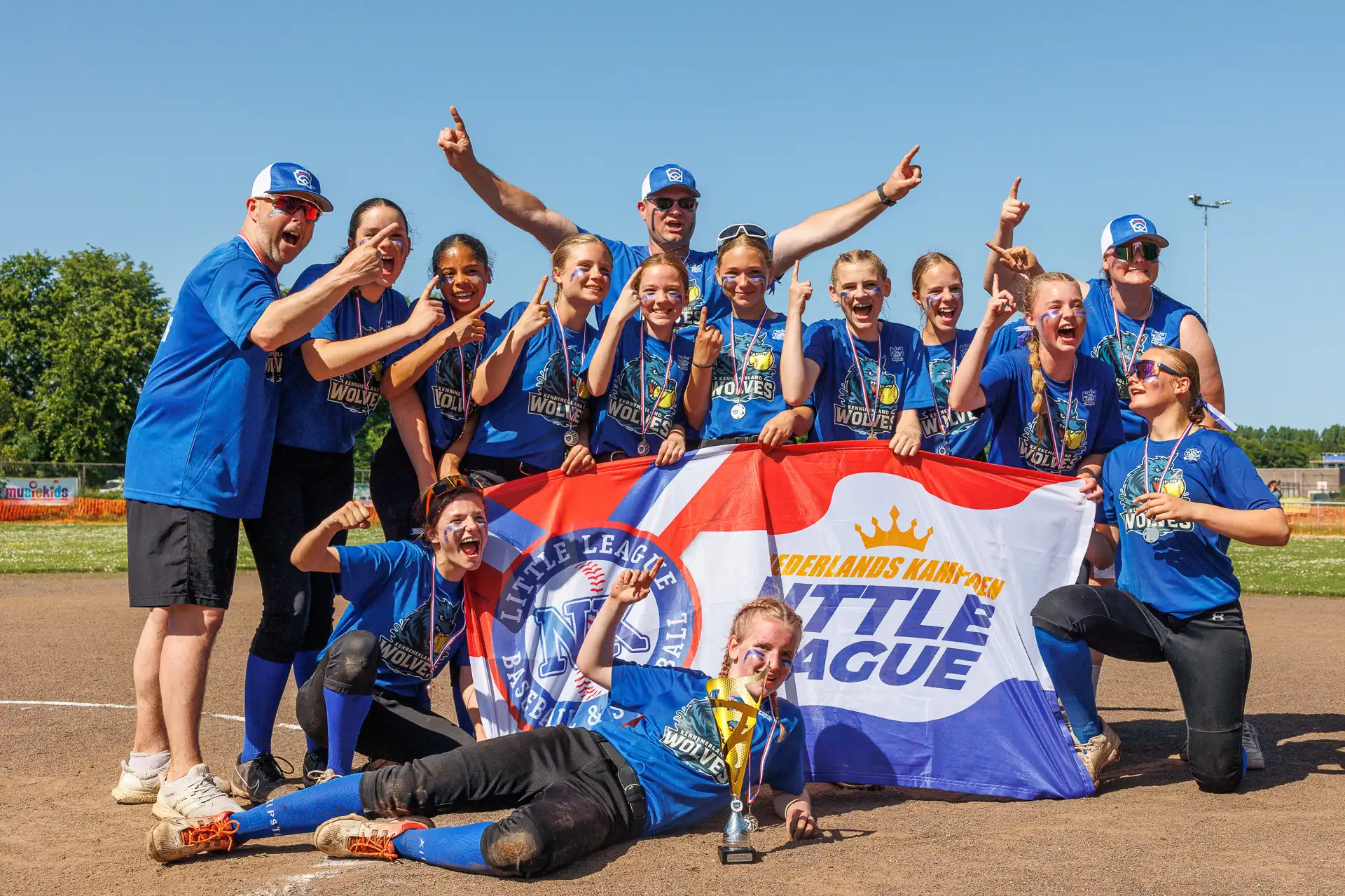 Softbalteam juicht achter de vlag met de tekst Nederlands Kampioen Little League
