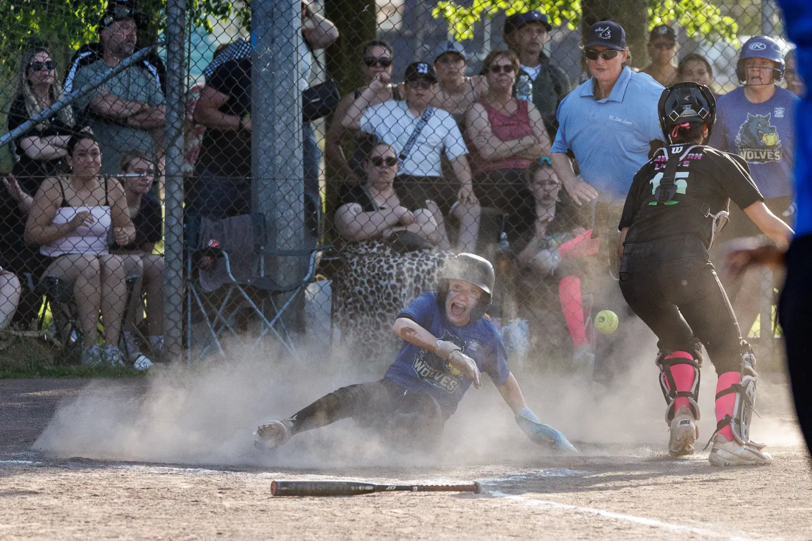 Softbalspeelster glijdt door een stofwolk naar de thuisplaat, publiek kijkt toe achter het hek