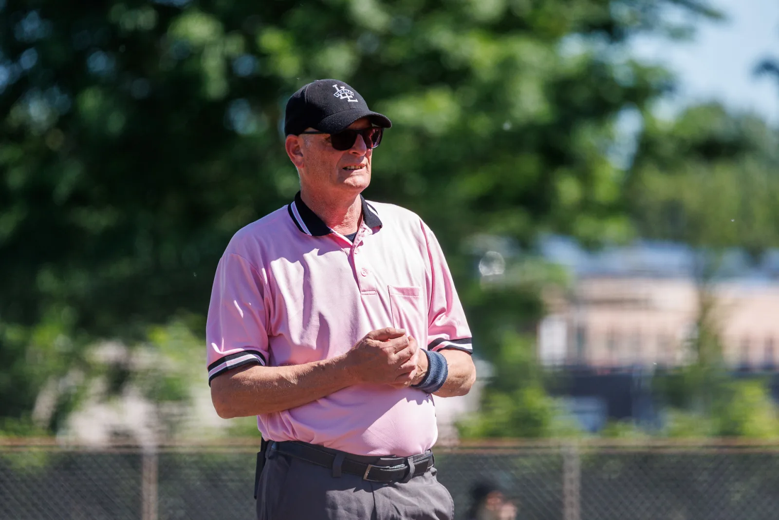 Een umpire in roze shirt met pet en zonnebril kijkt het veld in.
