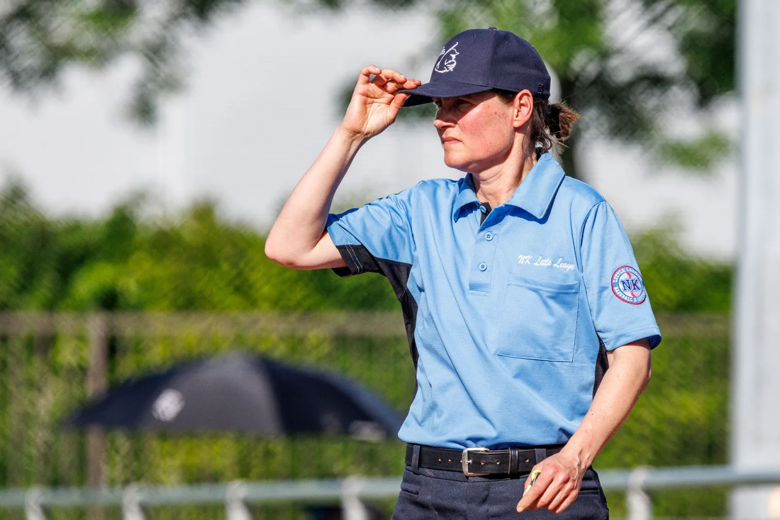 Een umpire in een lichtblauw shirt tikt haar pet aan terwijl ze het veld overziet.