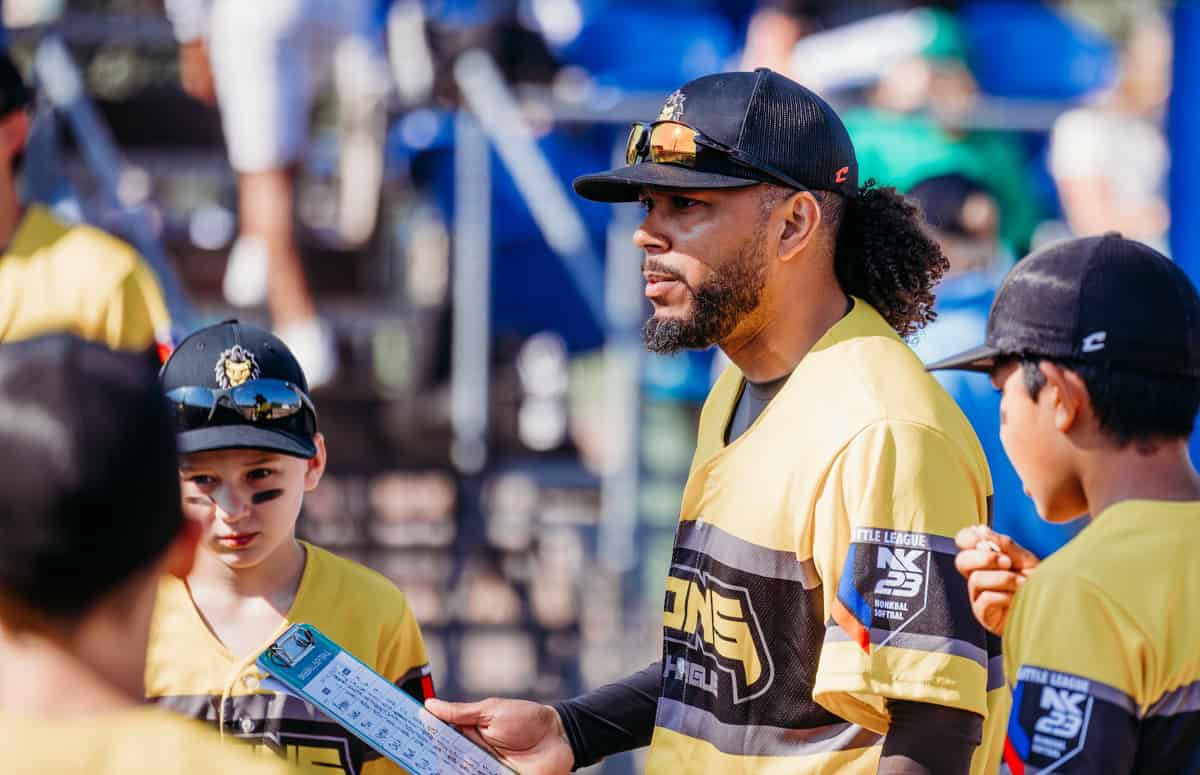 Veelzijdige sportcoach met kinderen op Little League toernooi, teamgeest en coaching in jeugdbaseball.