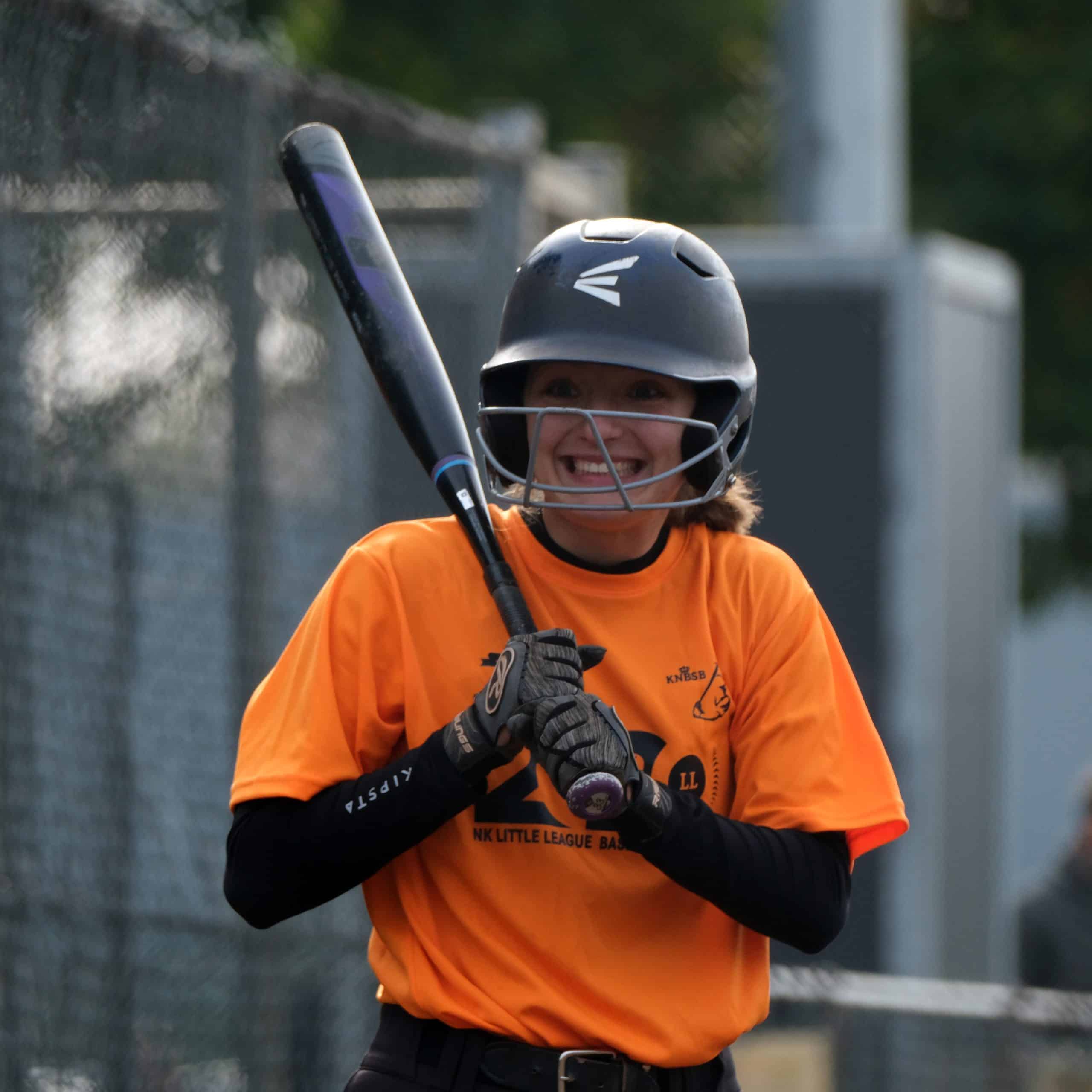 Joyvolle jeugdspeler met een honkbalhelm, klaar voor de wedstrijd bij Little League Nederland.
