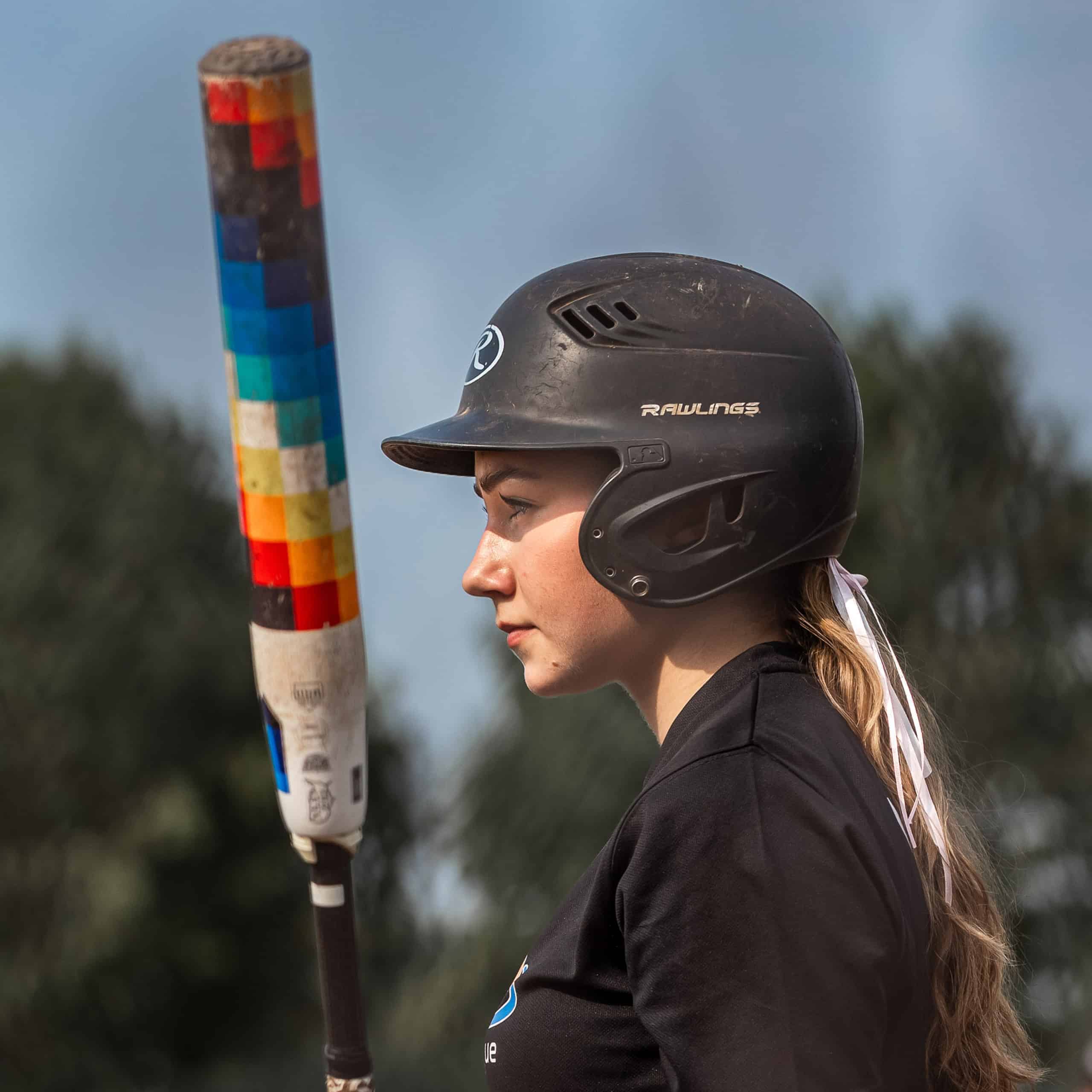 Momentopname van vrouw met honkbalhelm en bat tijdens Little League wedstrijd.